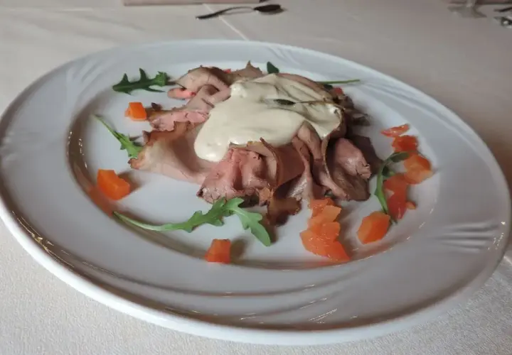 Vitello tonnato, un classico con origini piemontesi, servito su un piatto bianco con pomodorini e rucola.
