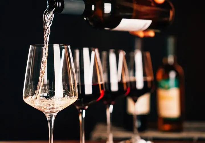 Versando vino bianco in un calice, con altri calici pieni di un intenso rosso rubino sullo sfondo.