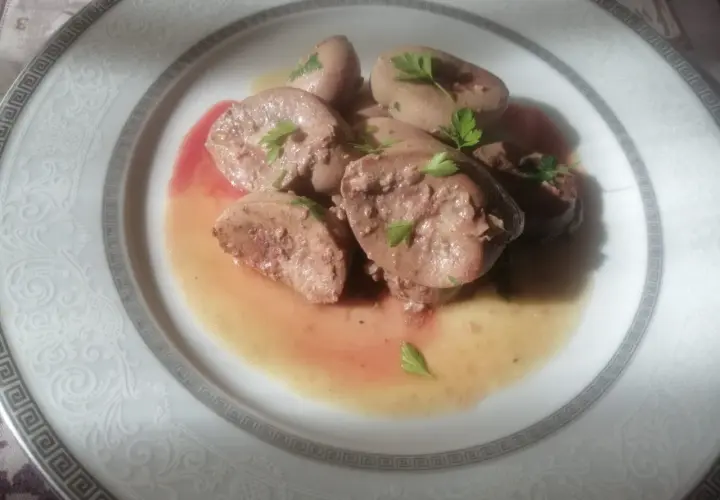 Piatto di rognone trifolato, guarnito con prezzemolo fresco, servito su un elegante piatto bianco con decorazioni in rilievo.