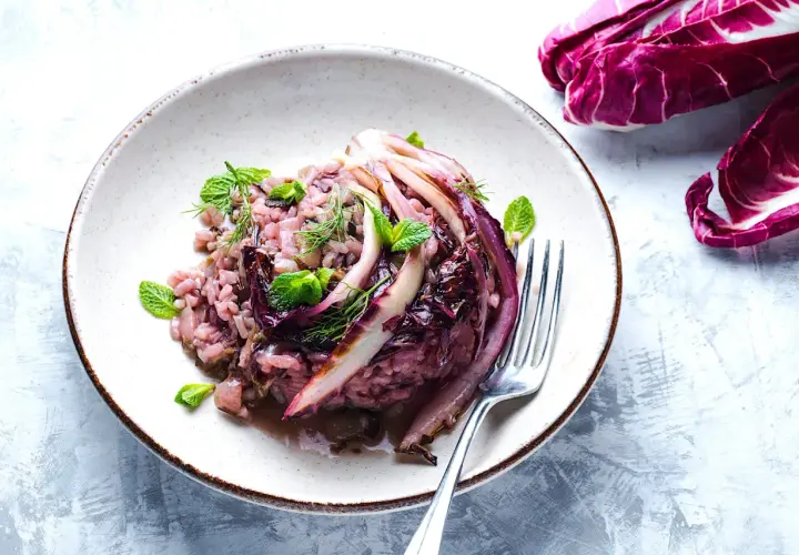 Un cremoso risotto al radicchio, guarnito con foglie di menta fresca e aneto, pronto per essere gustato.