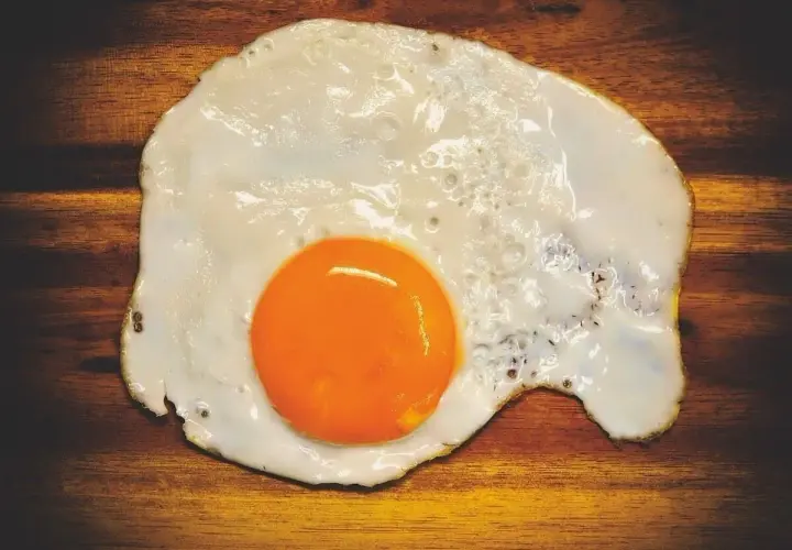 Un uovo in cereghin, cotto alla perfezione, con un tuorlo arancione brillante su un tagliere di legno scuro.