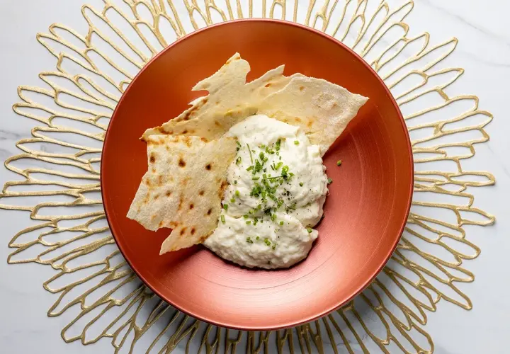Brandade di baccalà cremosa, guarnita con erba cipollina e pepe, servita con croccanti sfoglie di pane su un piatto ramato.