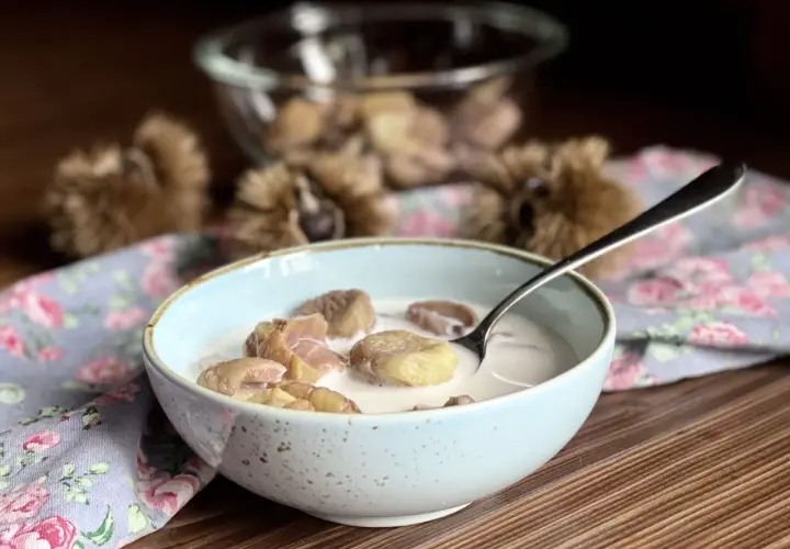 Una ciotola di castagne al latte, un dolce autunnale cremoso e confortante, con ricci di castagne sullo sfondo.