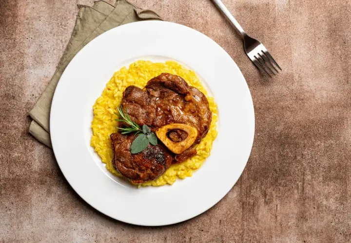 Ossobuco con risotto alla milanese, un classico dei piatti tipici Lombardia, guarnito con rosmarino e salvia.