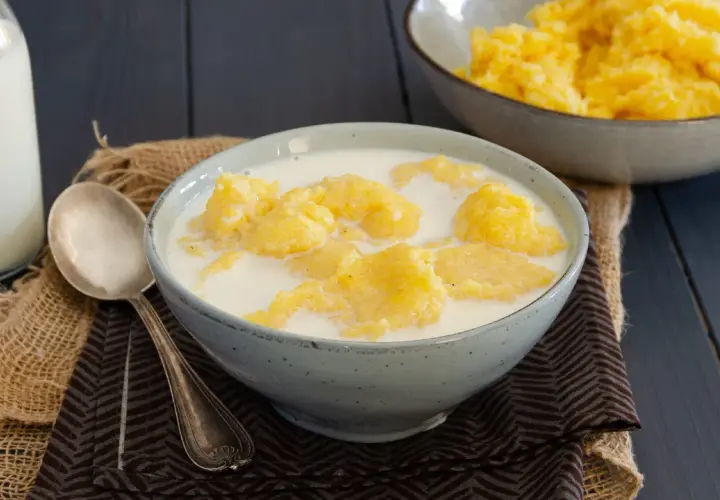 Una ciotola di polenta e latte, un piatto confortante. Accanto, una bottiglia di latte e un cucchiaio d'argento.