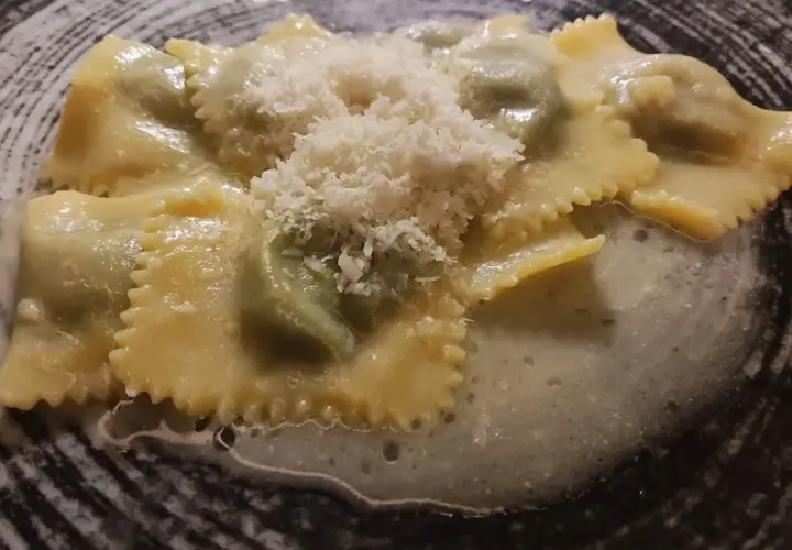 Ravioli italiani ripieni, conditi con una salsa cremosa e spolverati di parmigiano grattugiato, serviti in un piatto scuro.