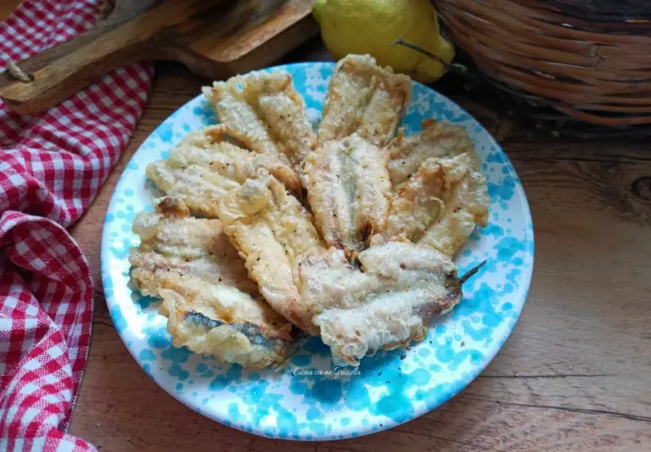 A plate of golden fried anchovies with a light, crispy coating, seasoned with pepper.