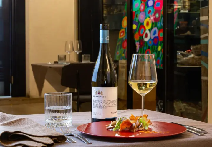 Un bicchiere di vino bianco Catarratto, con le sue caratteristiche freschezza e note agrumate, accompagna un piatto gourmet.