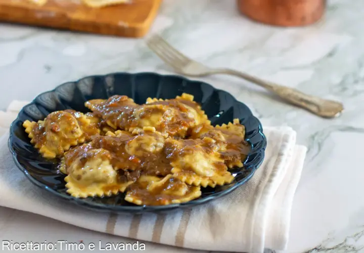 Piatto di agnolotti al brasato, conditi con un sugo ricco e saporito, serviti su un piatto scuro.