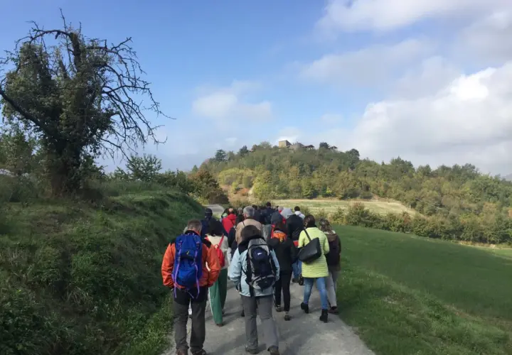 Gruppo di escursionisti sul sentiero delle fontane, con colline boscose e un borgo in cima.