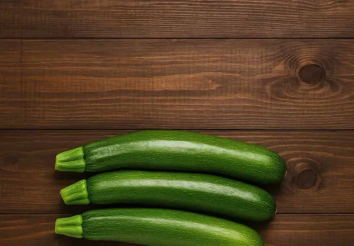 Tre zucchine fresche su un tavolo di legno scuro, pronte per fantastiche ricette con zucchine.