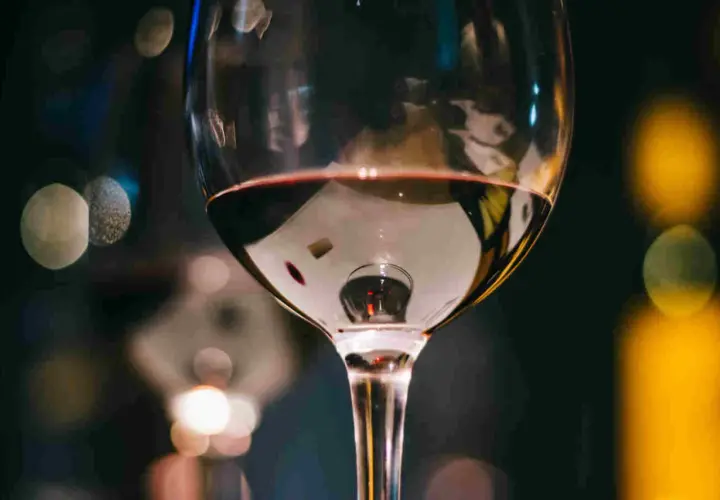 Un bicchiere di vino rosso riflette luci sfocate. Immagina tre bicchieri pronti per una degustazione serale.
