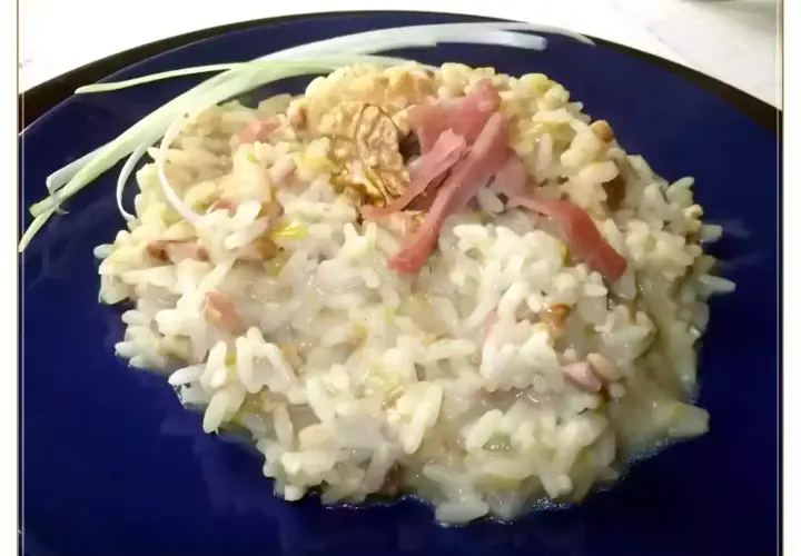 Un cremoso risotto pere e speck, guarnito con noci e fili di porro.