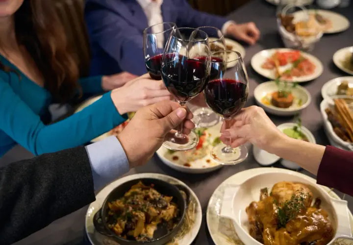 Brindisi con vino rosso, forse un Muller Thurgau, durante una cena conviviale con piatti invitanti.