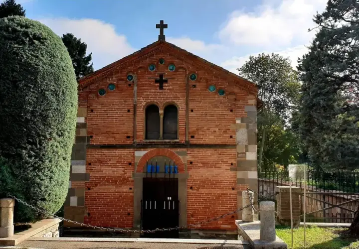 Chiesa in mattoni rossi con croce in cima, circondata da alberi verdi. Un luogo tranquillo, forse a Voghera dove si trova.