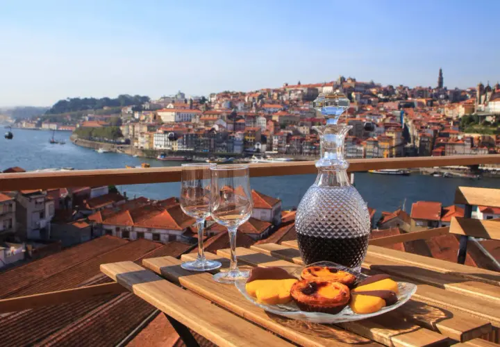 Un bicchiere di vino porto e dolci su un tavolo con vista sulla città di Porto, Portogallo.