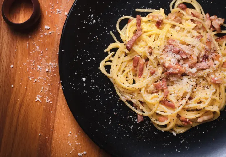 Spaghetti alla carbonara, un piatto che evoca la sua origine romana, con guanciale croccante e pecorino.