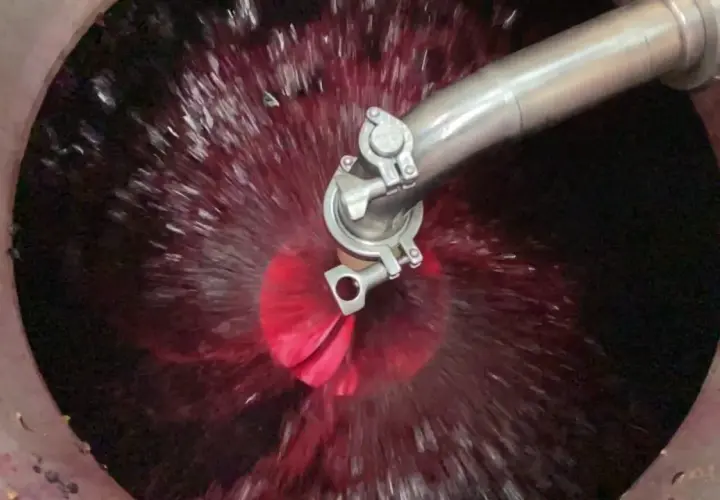 Il rimontaggio del vino in vasca, con il mosto rosso che vortica attorno a un ugello metallico.