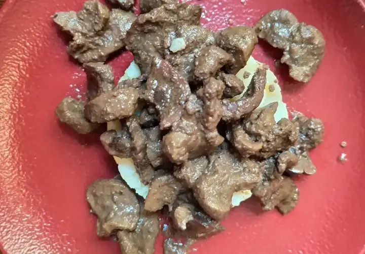 Un succulento piatto di frittura di maiale, servito su una base di patate, su un piatto rosso.