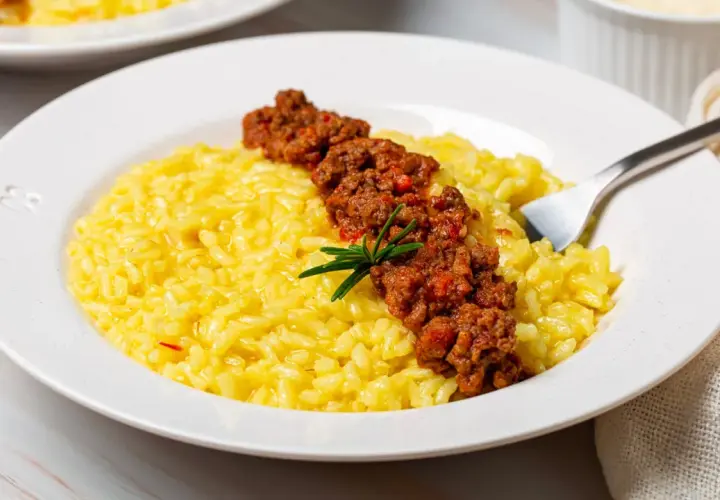Risotto giallo cremoso con ragù di salsiccia e stracchino, guarnito con rosmarino.