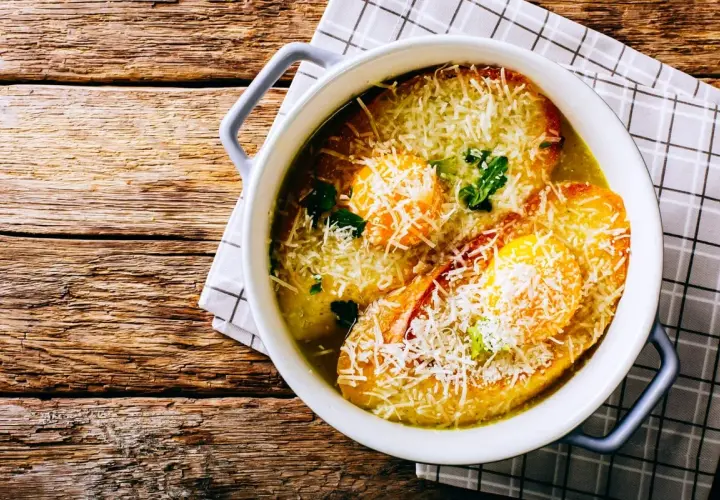 Zuppa alla pavese fumante, con pane tostato, uova e abbondante parmigiano grattugiato, servita in una ciotola bianca su un tavolo di legno rustico.