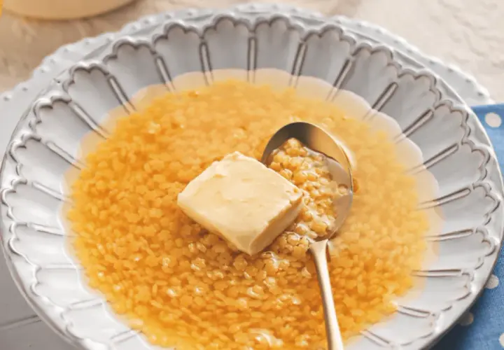 Minestrina in brodo con dado, un comfort food che scalda il cuore. Un cucchiaio d'oro raccoglie la pasta minuta e un cubetto di burro si scioglie nel brodo caldo.