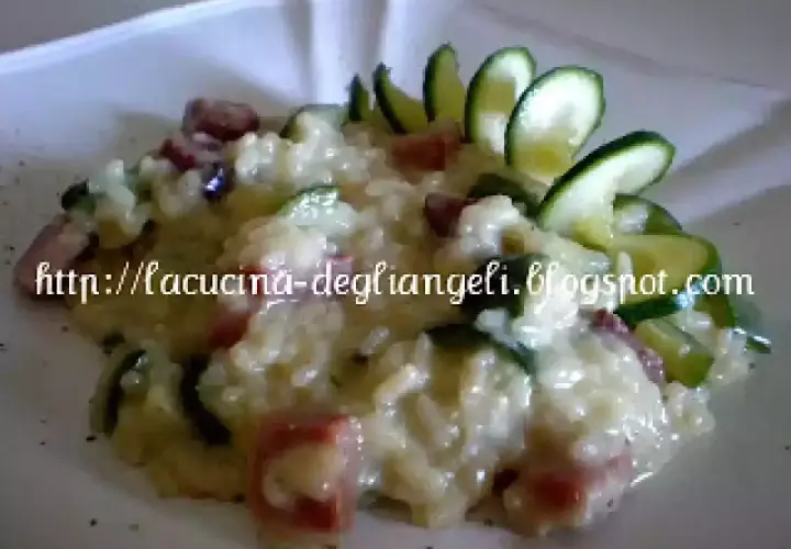 Risotto cremoso con robiola e speck croccante, guarnito con zucchine fresche. Un piatto delizioso e invitante.