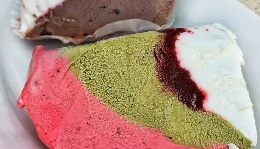 Un pezzo duro gelato a strati: rosa, verde pistacchio e bianco con striature rosse. Un altro pezzo di gelato al cioccolato e bianco è sullo sfondo.