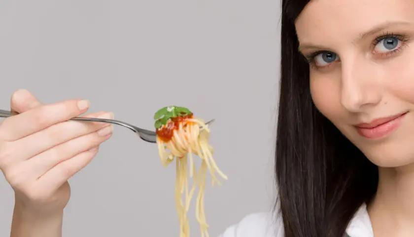 Donna con forchettata di spaghetti al pomodoro, un piatto che sembra quasi un'opera d'arte con i suoi formati di pasta strani e invitanti.
