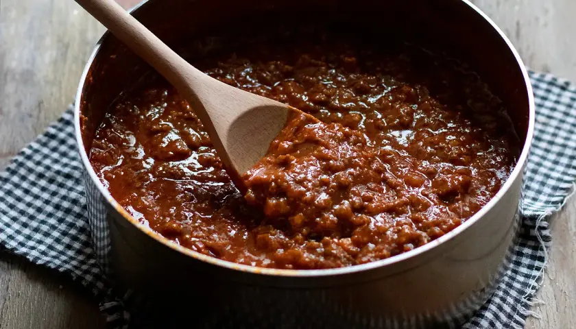 Un pentolone pieno di ragù, pronto per condire gli spaghetti. Un cucchiaio di legno mescola la salsa.