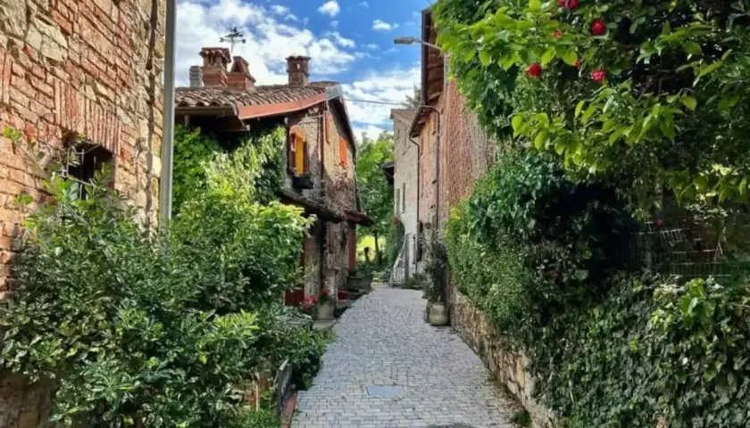 Un vicolo acciottolato nel Val di Nizza, con case in pietra ricoperte di edera e rose rosse.