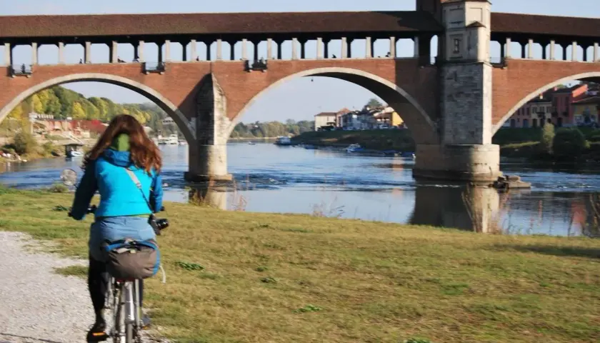 Ciclista sulla ciclabile Milano Pavia, con il Ponte Coperto di Pavia sullo sfondo.
