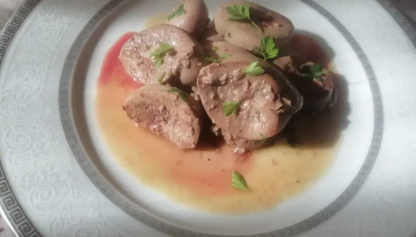 Piatto di rognone trifolato, guarnito con prezzemolo fresco, servito su un elegante piatto bianco con decorazioni in rilievo.