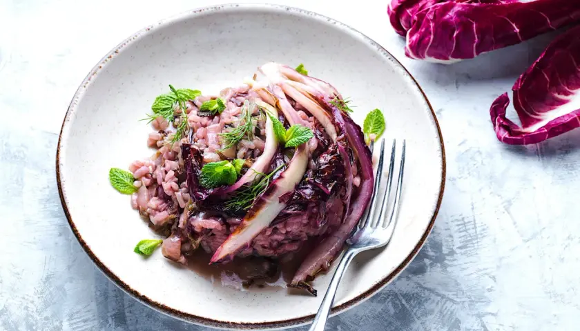 Un cremoso risotto al radicchio, guarnito con foglie di menta fresca e aneto, pronto per essere gustato.