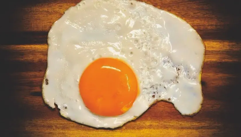 Un uovo in cereghin, cotto alla perfezione, con un tuorlo arancione brillante su un tagliere di legno scuro.