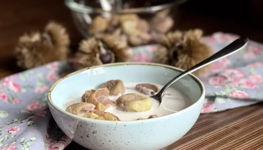 Una ciotola di castagne al latte, un dolce autunnale cremoso e confortante, con ricci di castagne sullo sfondo.