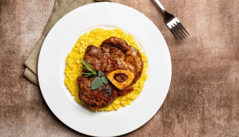Ossobuco con risotto alla milanese, un classico dei piatti tipici Lombardia, guarnito con rosmarino e salvia.
