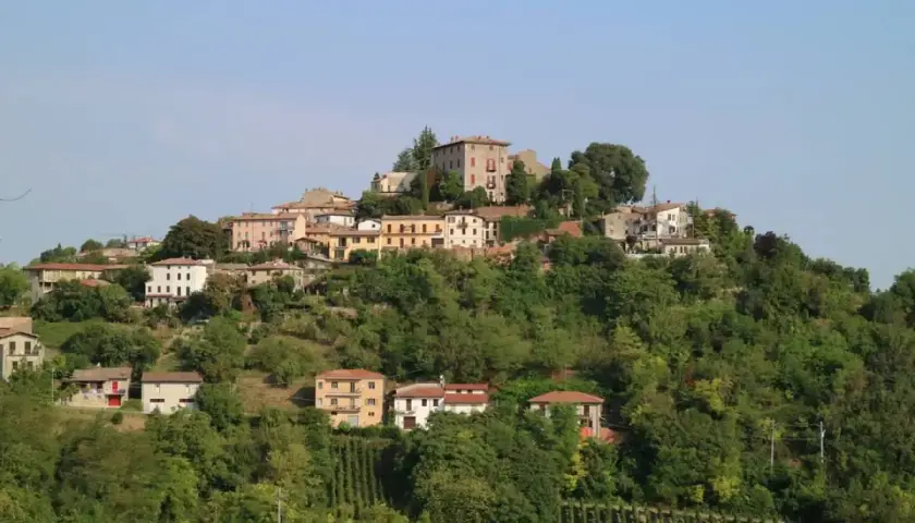 Borgo collinare di Montu Beccaria, con case colorate e vigneti rigogliosi sotto un cielo azzurro.