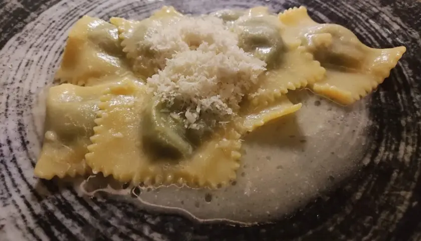 Ravioli italiani ripieni, conditi con una salsa cremosa e spolverati di parmigiano grattugiato, serviti in un piatto scuro.