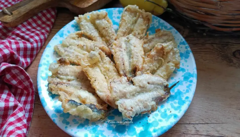 A plate of golden fried anchovies with a light, crispy coating, seasoned with pepper.