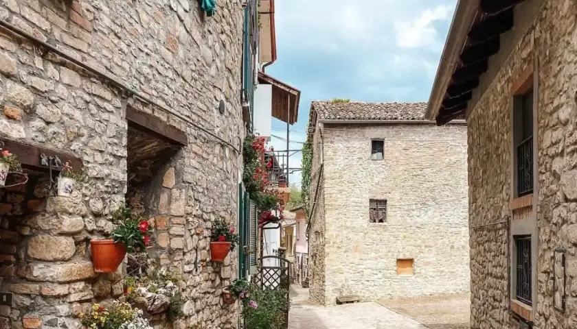 Un vicolo tra antichi borghi in provincia di Pavia, con case in pietra e vasi di fiori colorati che adornano i muri.