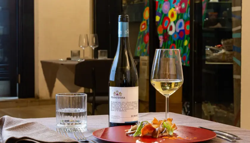 Un bicchiere di vino bianco Catarratto, con le sue caratteristiche freschezza e note agrumate, accompagna un piatto gourmet.
