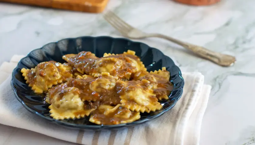 Piatto di agnolotti al brasato, conditi con un sugo ricco e saporito, serviti su un piatto scuro.