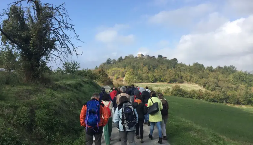 Gruppo di escursionisti sul sentiero delle fontane, con colline boscose e un borgo in cima.