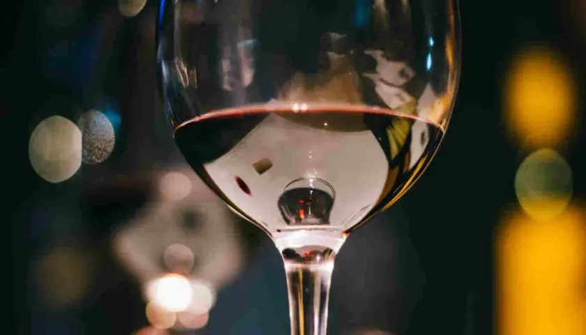 Un bicchiere di vino rosso riflette luci sfocate. Immagina tre bicchieri pronti per una degustazione serale.