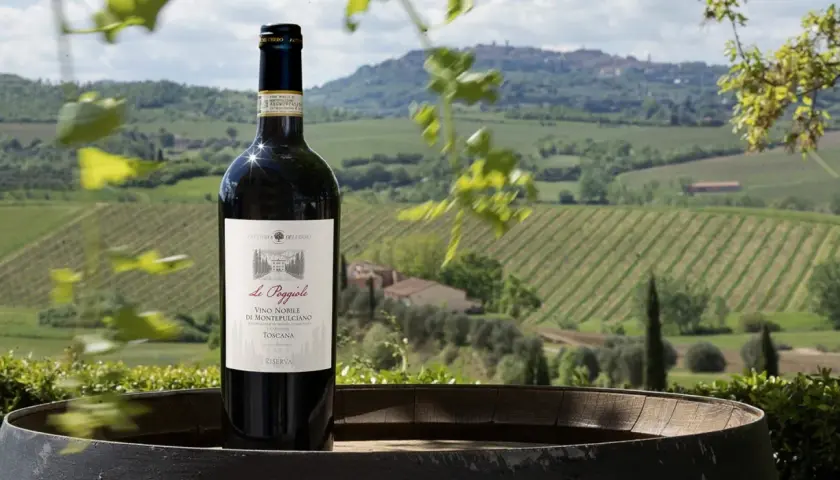 Bottiglia di Vino Nobile di Montepulciano in primo piano, con vigneti e colline toscane sullo sfondo.
