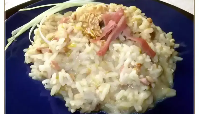 Un cremoso risotto pere e speck, guarnito con noci e fili di porro.