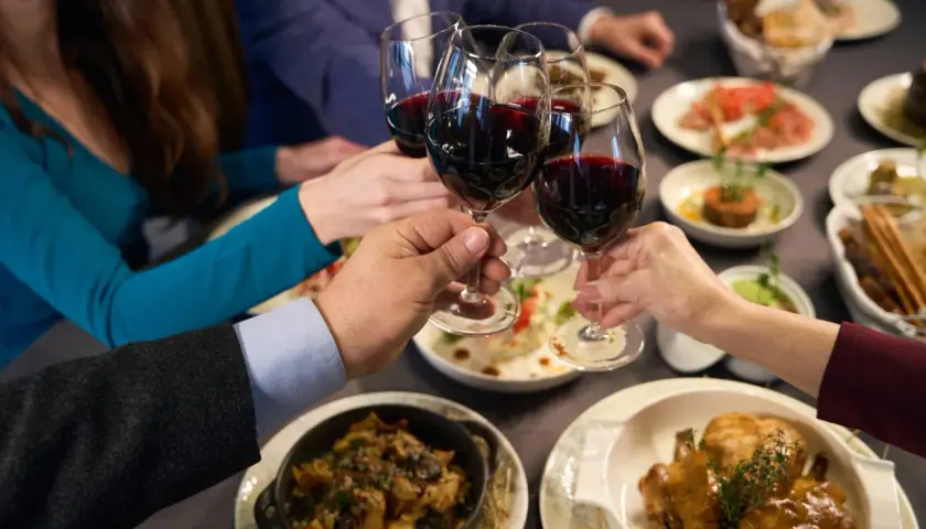 Brindisi con vino rosso, forse un Muller Thurgau, durante una cena conviviale con piatti invitanti.