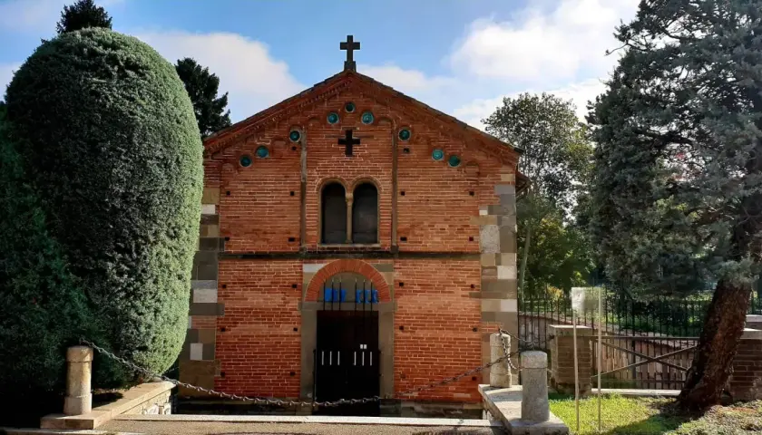 Chiesa in mattoni rossi con croce in cima, circondata da alberi verdi. Un luogo tranquillo, forse a Voghera dove si trova.