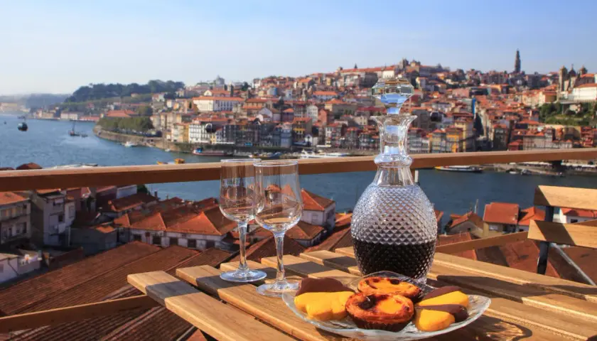 Un bicchiere di vino porto e dolci su un tavolo con vista sulla città di Porto, Portogallo.